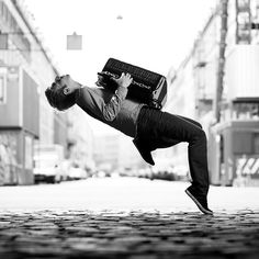 a man is doing a handstand on the street with a suitcase over his head