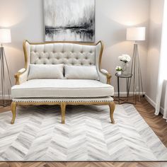 a white couch sitting on top of a wooden floor next to two lamps and a painting