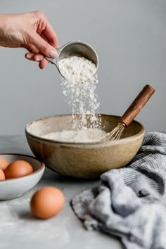 someone sprinkling flour into a bowl with eggs in the background