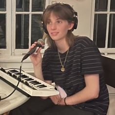 a woman sitting in front of a keyboard with headphones on and holding a microphone