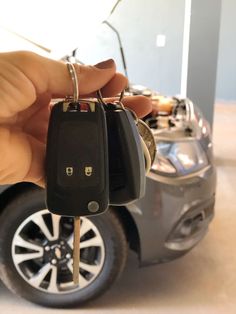 a hand holding two car keys in front of a vehicle