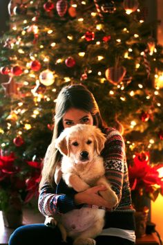 a woman holding a dog in front of a christmas tree