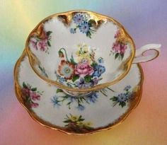 two tea cups and saucers sitting on top of a rainbow colored tablecloth with gold trim