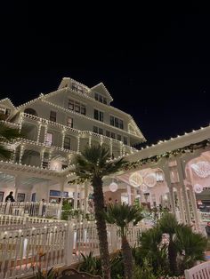 a large white house with christmas lights on it's sides and palm trees in the foreground