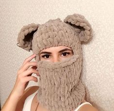 a woman wearing a knitted bear mask with ears on her head and hands in front of her face