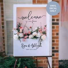 a welcome sign with flowers on it in front of a brick building