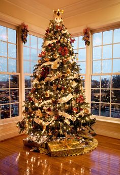 a decorated christmas tree in a living room with large windows and wooden flooring on the side