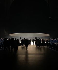 a group of people standing in front of a large circular object at the end of a dark room