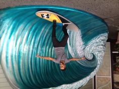 a man standing on a surfboard in front of a large wave sculpture that is painted blue and yellow