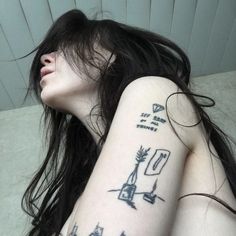 a woman with tattoos on her arm and shoulder is laying down next to a wall