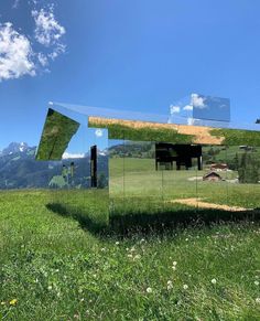 a mirror sitting on top of a lush green field under a blue sky with clouds