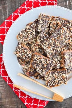 a white plate topped with brownies covered in nuts next to two wooden spoons