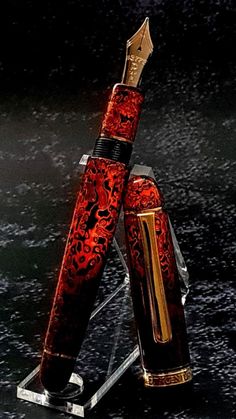 a red and gold fountain pen sitting on top of a glass stand in the dark