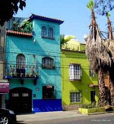 a blue and green building with palm trees in the foreground on a sunny day