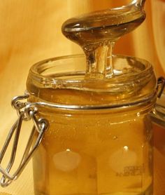 a glass jar filled with liquid sitting on top of a wooden table next to a spoon