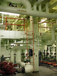 pipes and pipters in a large industrial facility with workers working on them, while another worker stands at the far end of the pipe