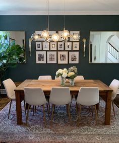 a dining room table with white chairs and pictures on the wall above it, along with a rug