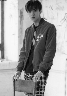 black and white photograph of a young man in plaid pants leaning on a wooden chair