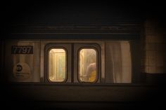 two windows on the side of a subway car at night with light coming from them