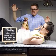 a woman laying on top of a counter next to a man with glasses and a sign