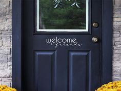 two yellow flowers sitting in front of a black door with the words welcome friends written on it