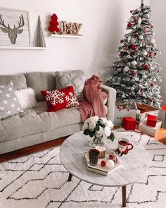 a living room decorated for christmas with white and red decorations on the walls, coffee table in front of a gray couch