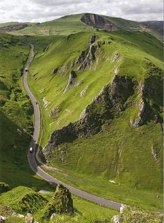 a car driving down a road in the middle of a green mountain range with rocks and grass on both sides