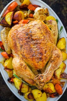 a roasted turkey with potatoes and carrots on a white platter, ready to be served