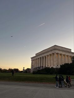 people walking in front of the lincoln memorial at sunset, with an airplane flying overhead