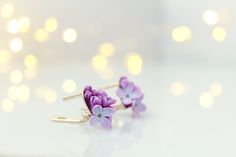 two purple flowers are sitting on top of some gold ear wires, with lights in the background