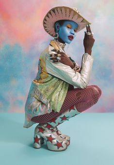 a woman with blue skin and makeup sitting on top of a white shoe wearing a hat