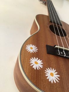 a ukulele with daisies painted on the fret and strings, sitting on a table