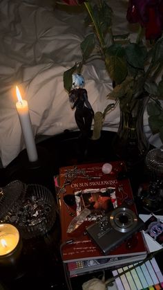 a table topped with books and candles next to a vase filled with flowers on top of a bed