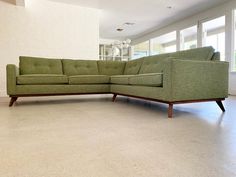 a green sectional couch sitting on top of a hard wood floor next to a window