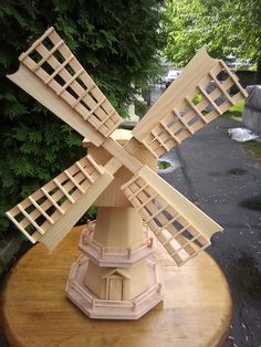 a wooden model of a windmill sitting on top of a table next to some trees