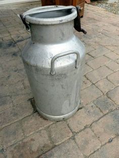 a large metal jug sitting on top of a brick sidewalk next to a building with a door