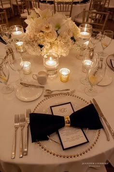 the table is set with silverware, candles and white flowers in centerpieces