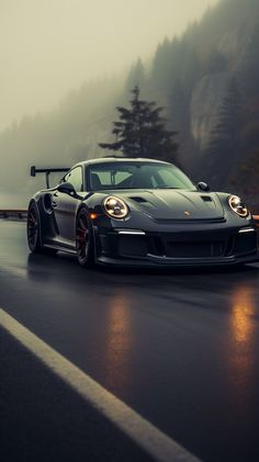 a black sports car driving down a road in the rain with foggy mountains behind it