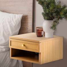 a nightstand with a vase and candle on it in front of a bed, next to a night stand