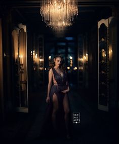 a woman standing in a dark room with a chandelier hanging from the ceiling