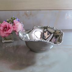 a silver bowl sitting on top of a counter next to a vase filled with flowers