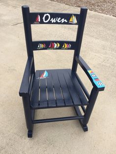 a black wooden chair sitting on top of a cement ground next to a sidewalk and trees