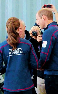 two people in blue jackets are talking to each other while others take pictures with their cell phones