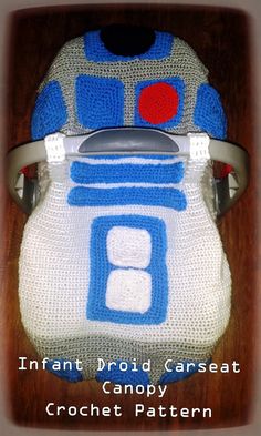 a crocheted hat with a blue and white robot design on the front, sitting on top of a chair