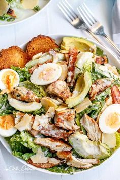 a white plate topped with salad next to two plates of fried eggs and other food