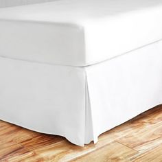 a white bed skirt on top of a wooden floor