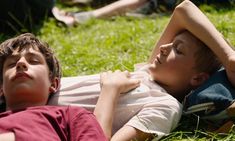 two young boys laying on the grass with their arms around each other and eyes closed