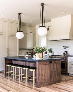 a kitchen island with stools and lights hanging over it