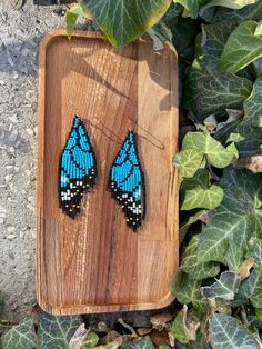 a pair of blue and black beaded earrings sitting on top of a wooden board