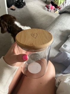 a woman holding up a glass container with a heart on the lid in front of her